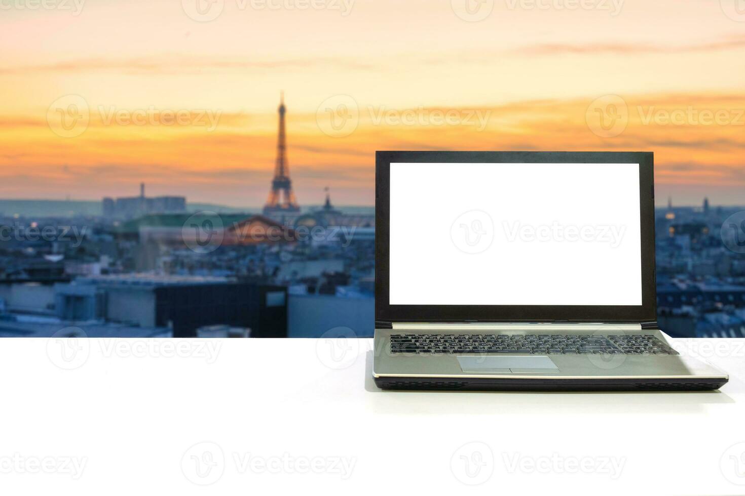 Laptop on white desk with blurred eiffel tower in paris at sunset photo