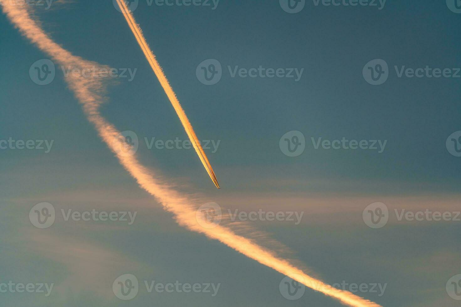 Airplane flying with condensation trails or contrail on the sky in the sunset photo