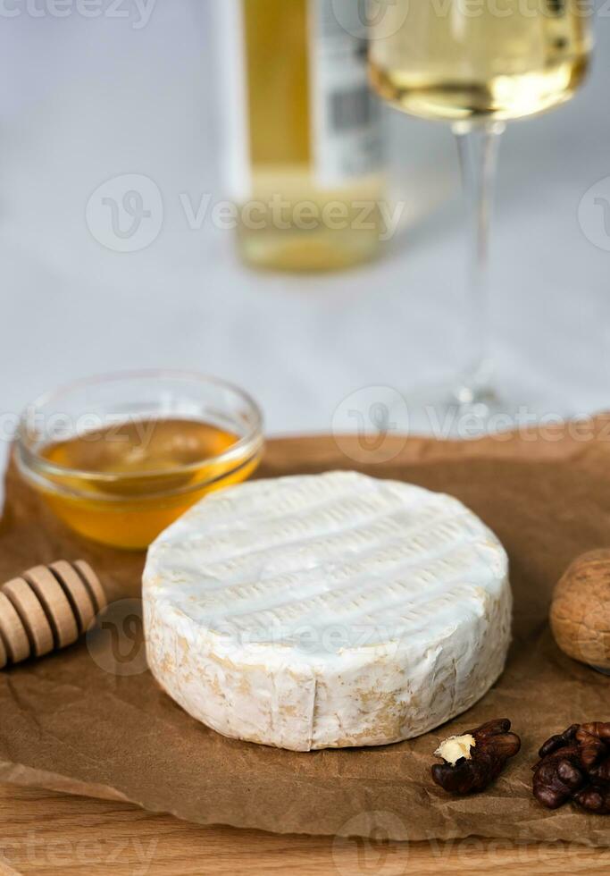 Soft cheese with white mold Camembert, honey, nuts and a glass of wine and a bottle of wine in the background. Close-up. Selective focus. photo