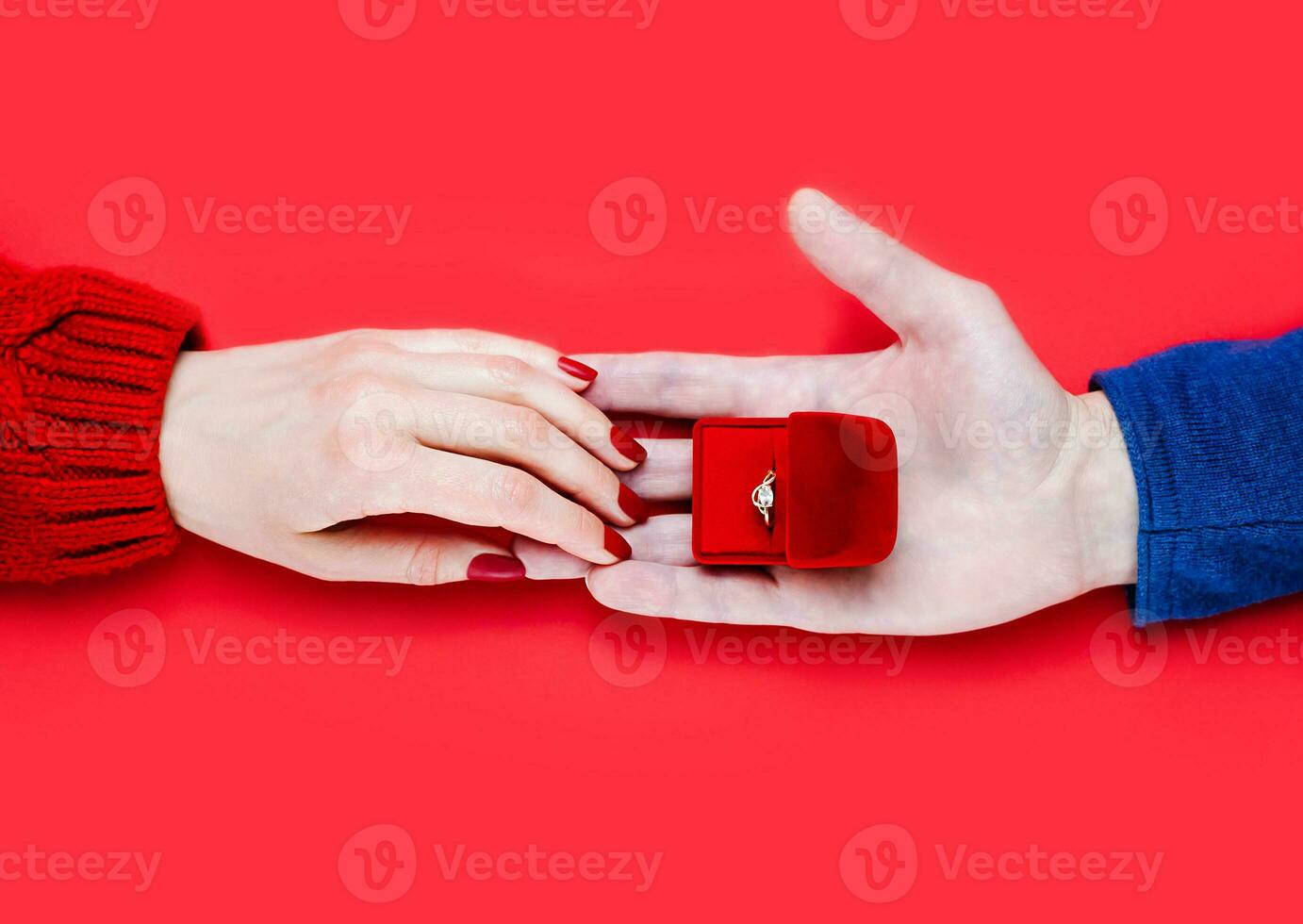 Man making marriage proposal. Male hand giving a gift box with engagement ring on red background. Close-up. Top view. photo