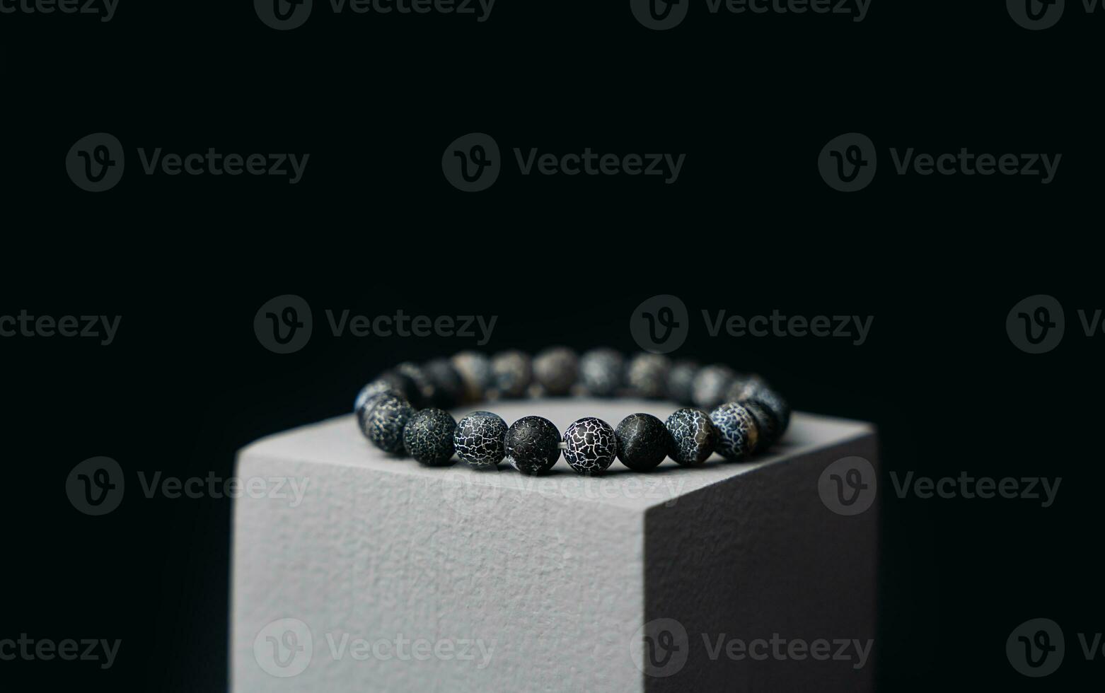 Natural stone bracelet on a gray podium on a black background. Close-up. photo