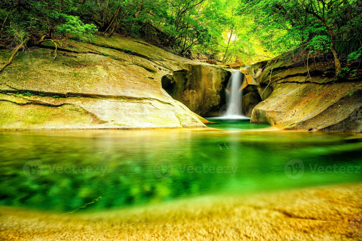 The photo displays a tranquil natural environment with a gorgeous waterfall, glistening water, rocky outcroppings, lush vegetation, and a deep forest in the distance