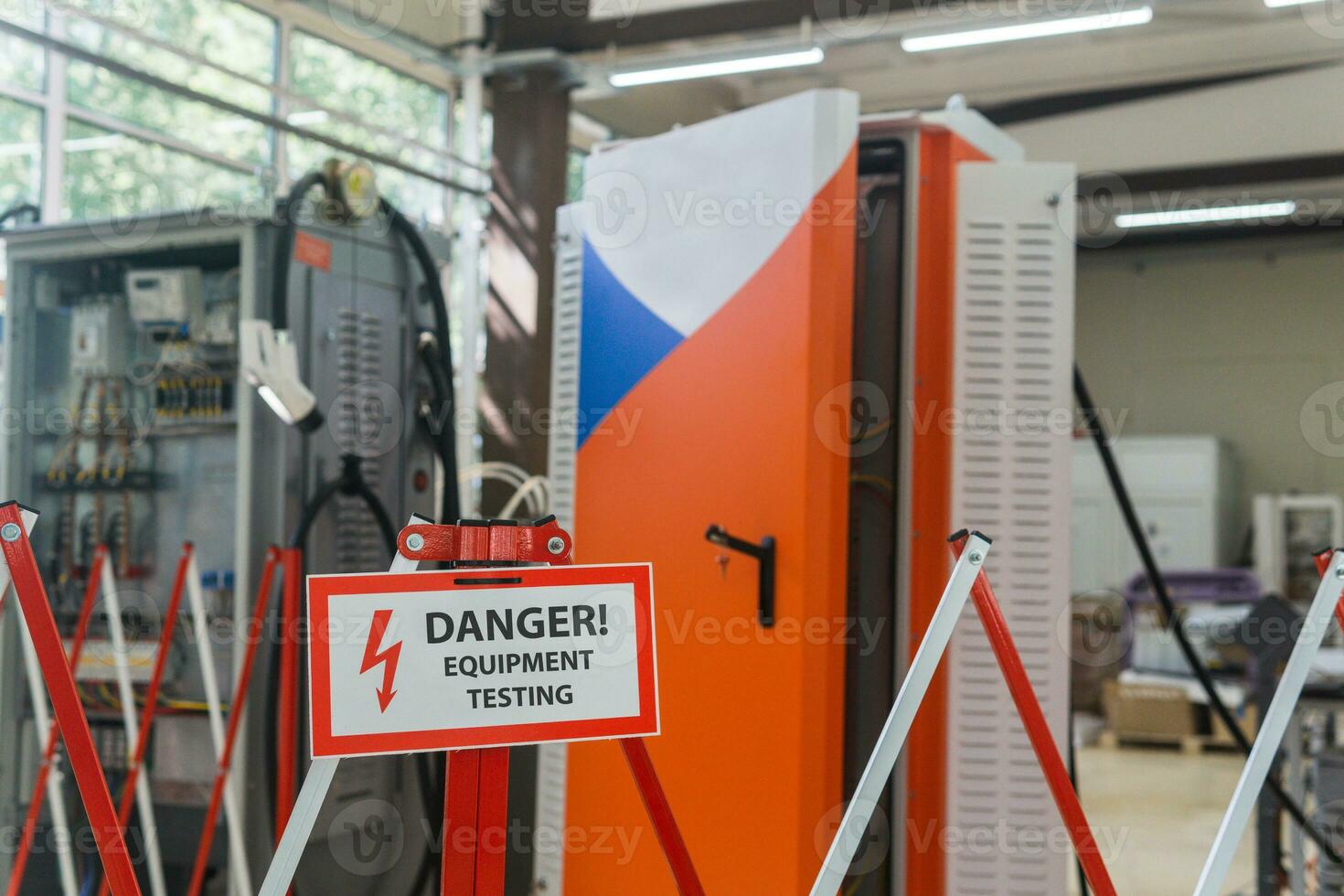 sign with the inscription Danger Equipment testing on the fence against the background of blurred electrical facilities in the workshop photo