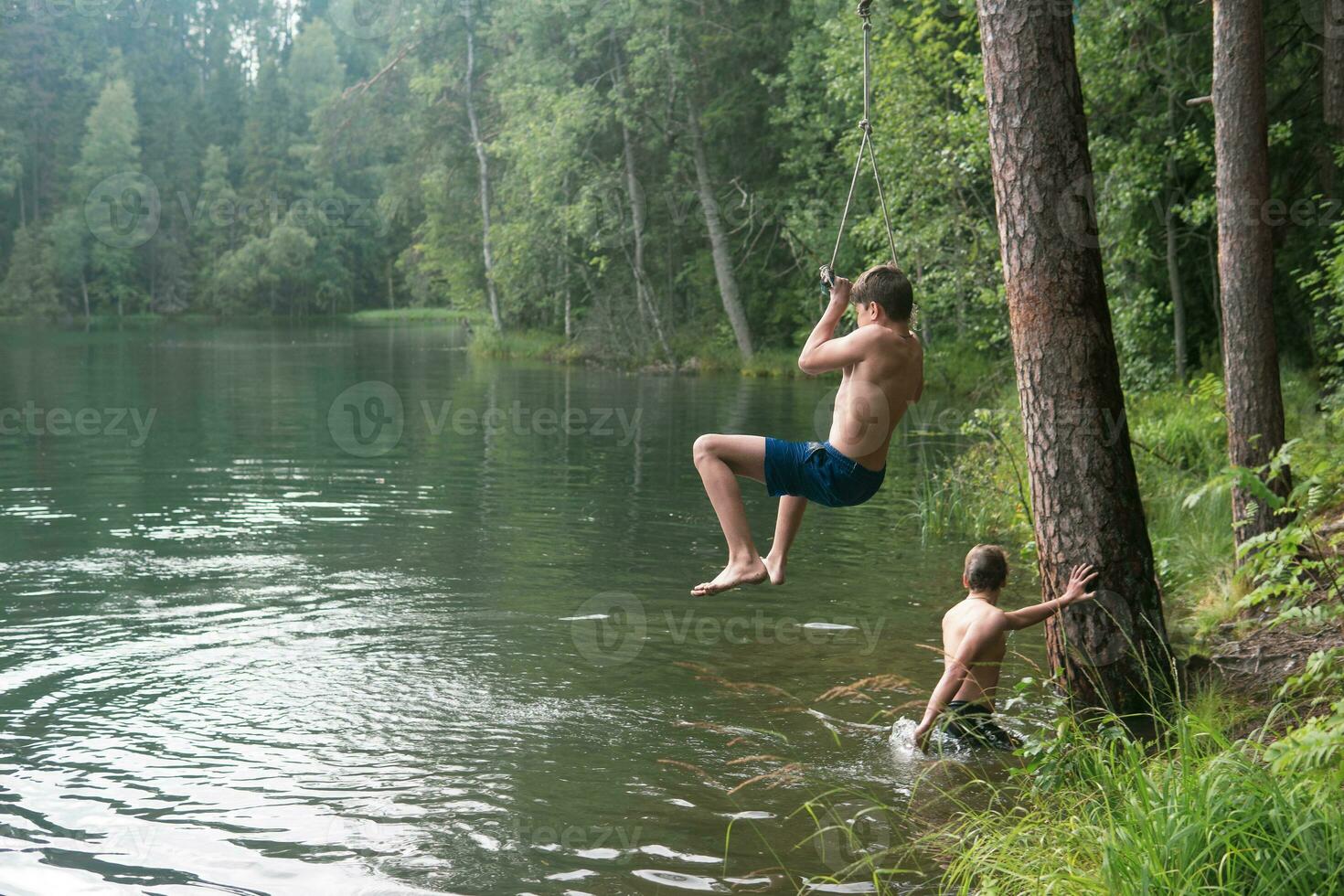 boys jumps into the water using a tarzan swing while swimming in a forest lake photo