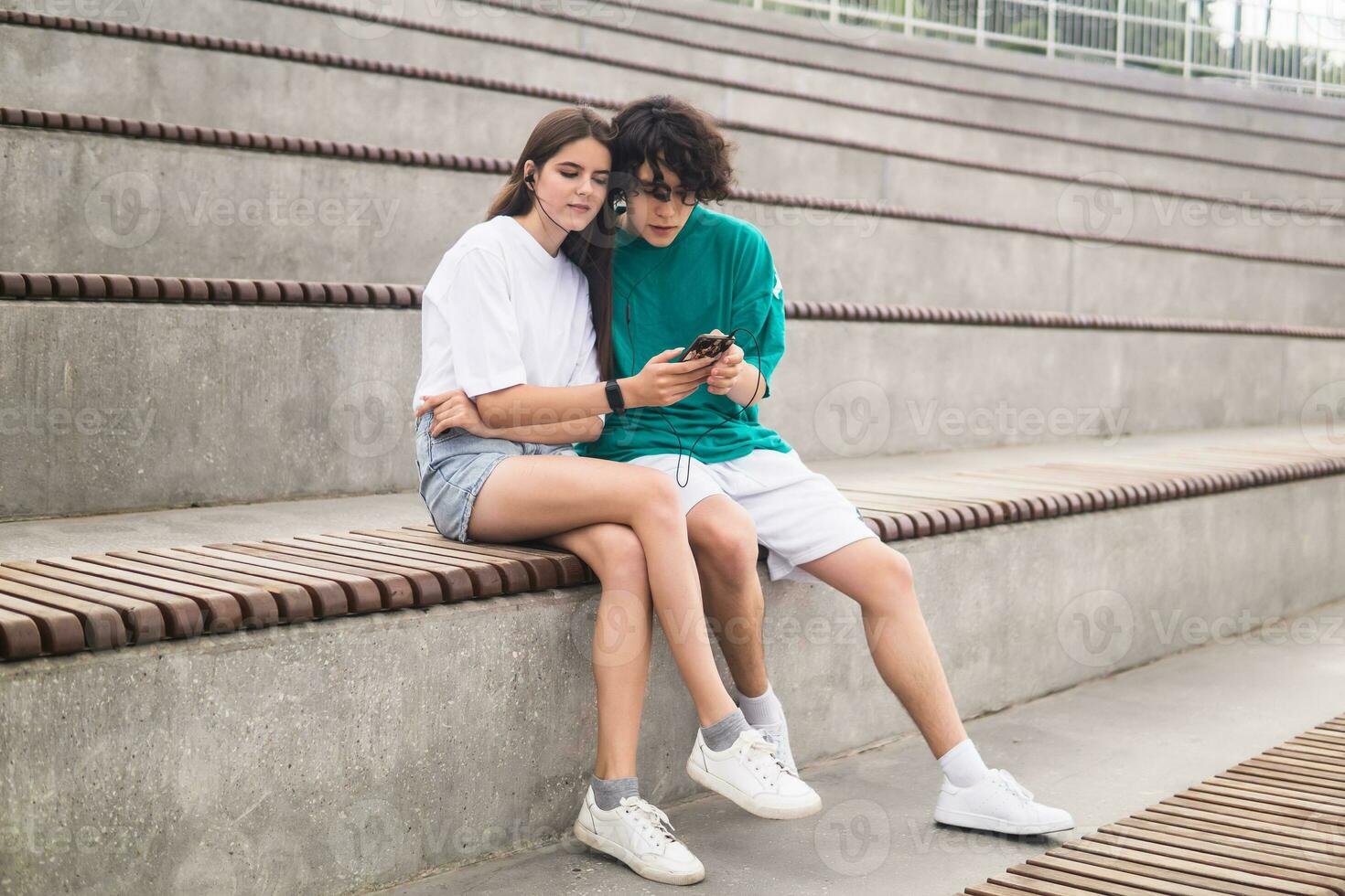 young couple together listening to the same music through headphones, sitting in empty stands photo