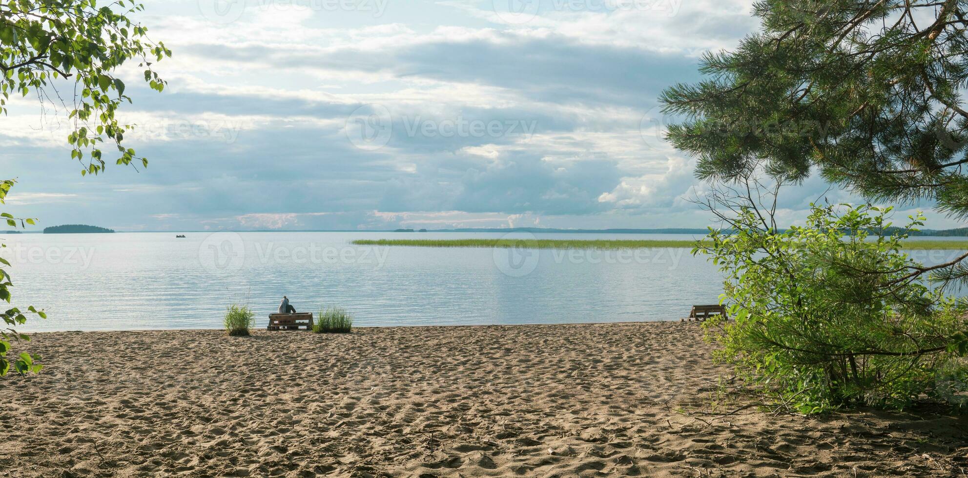 sandy beach on the shore of a vast lake, a female tourist is sitting on a bench made of old pallets photo