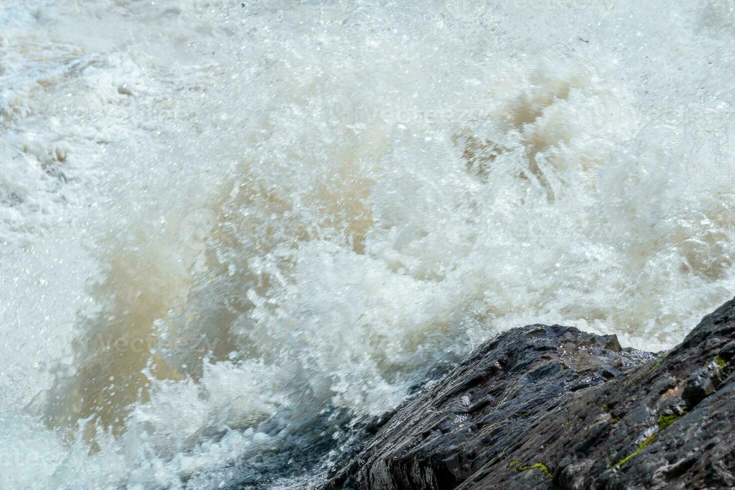 lodoso turbulento corriente debajo un rock durante alto agua foto