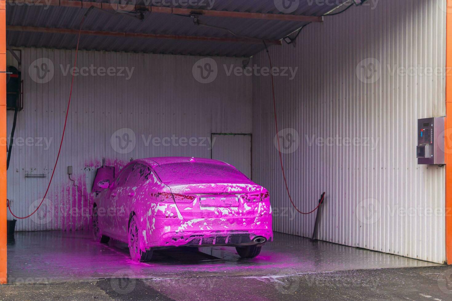 automobile at self service car wash covered with pink car shampoo