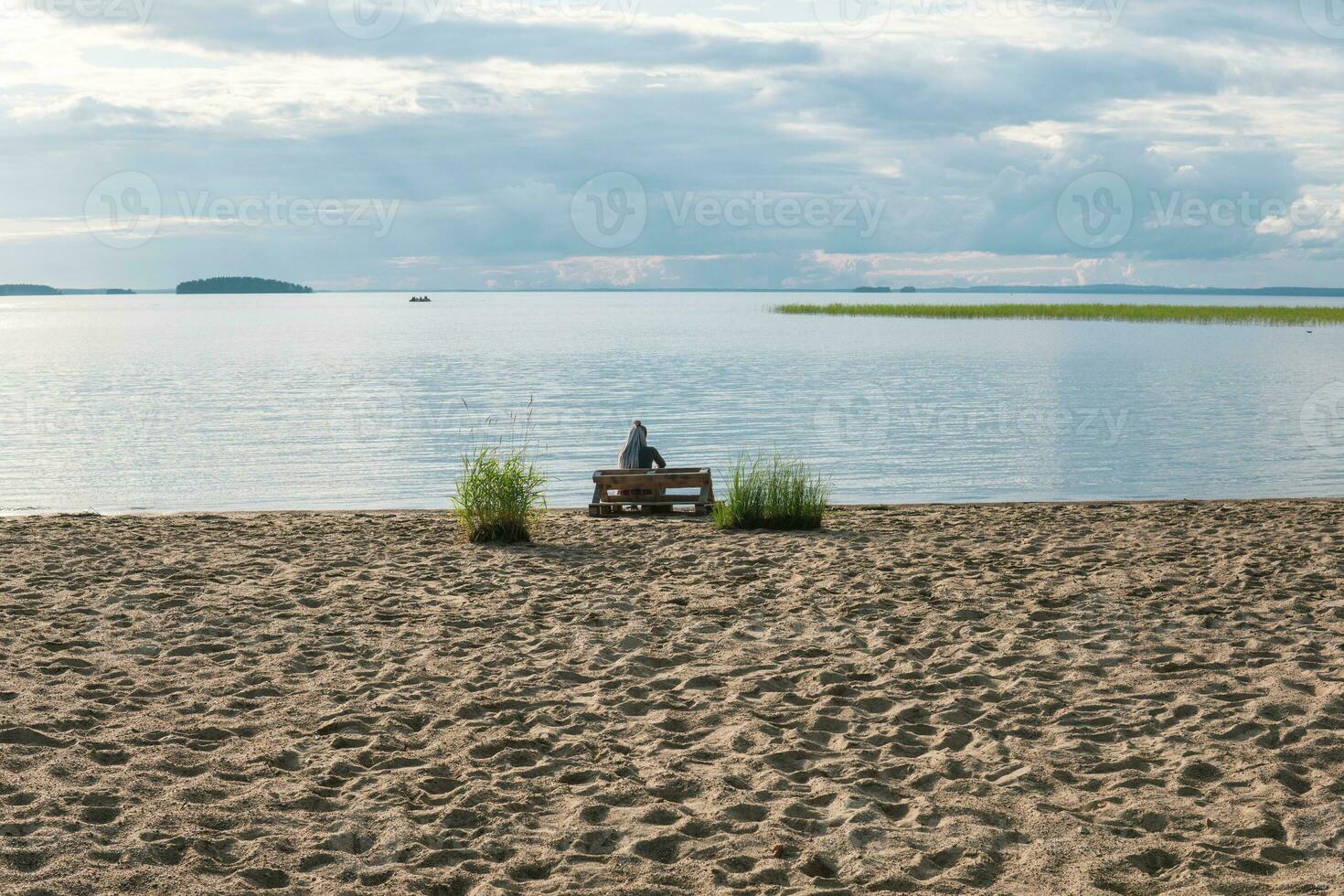 sandy beach on the shore of a vast lake, a woman traveler is sitting on a bench made of old pallets photo