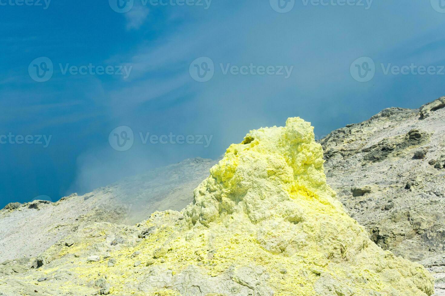 cone of sulfur deposits around a fumarole in a solfataric field against a blue sky photo