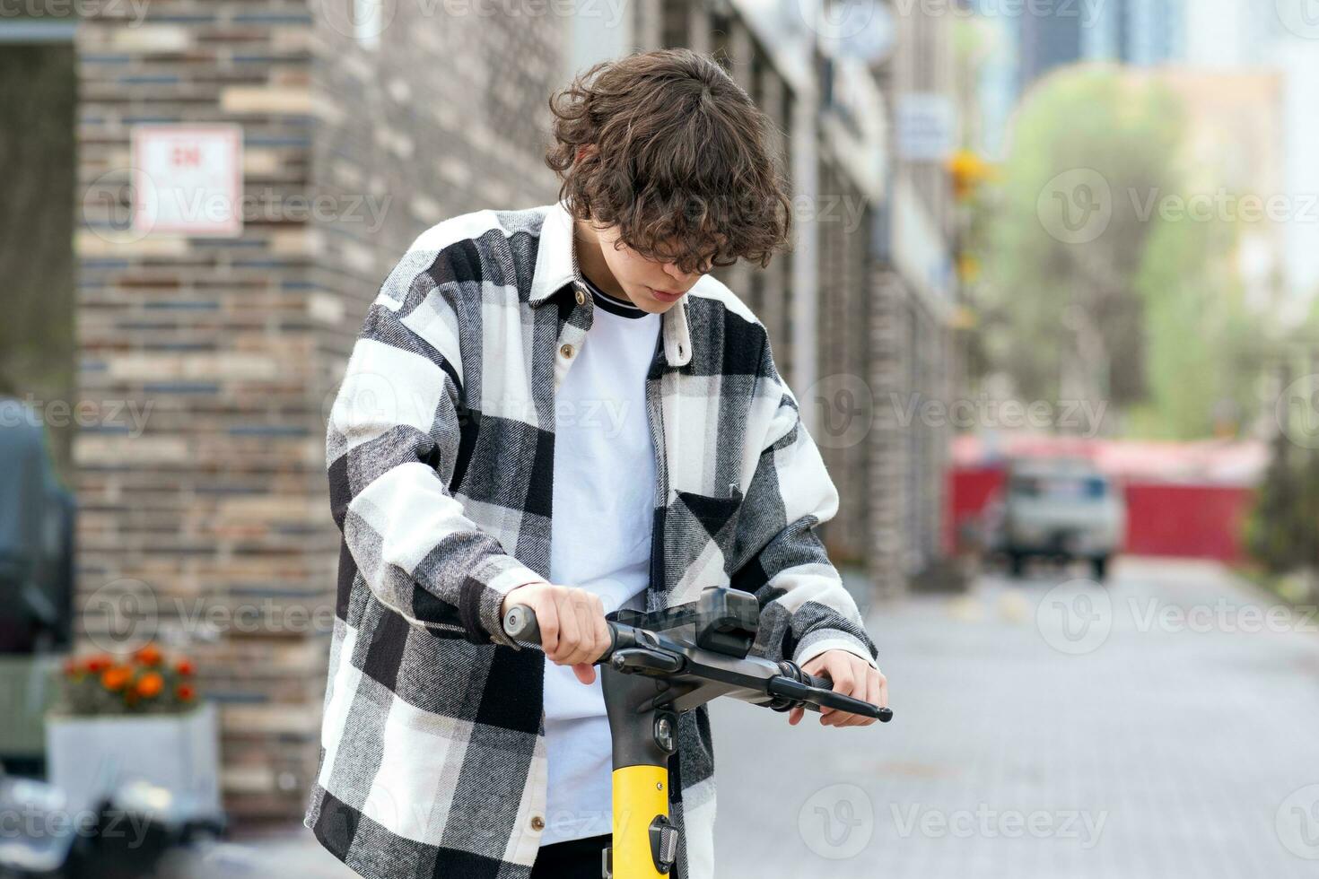 young man rides an electric scooter, looking at the application on a smartphone photo