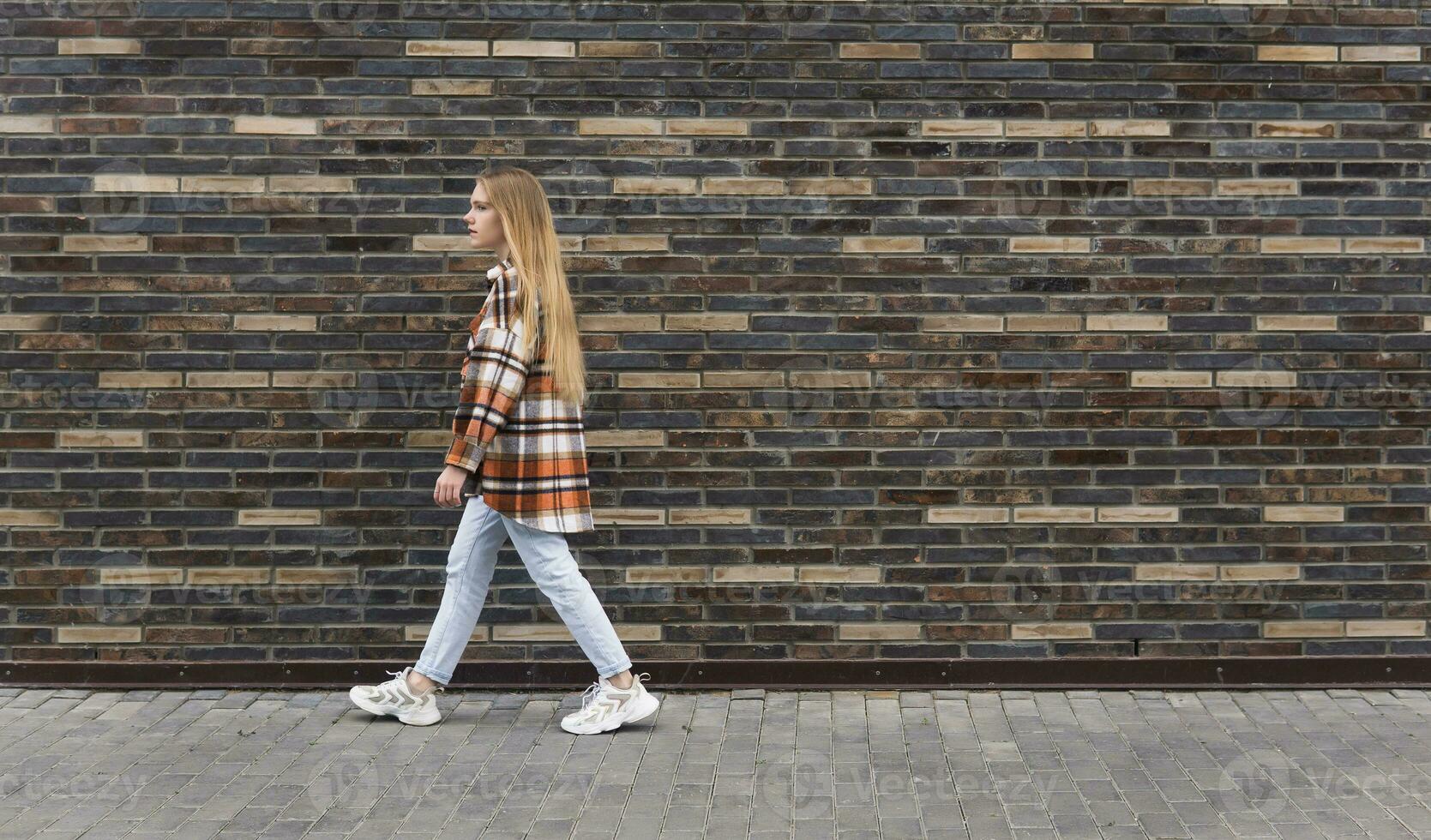 young woman walks down the street in front of a brick wall photo