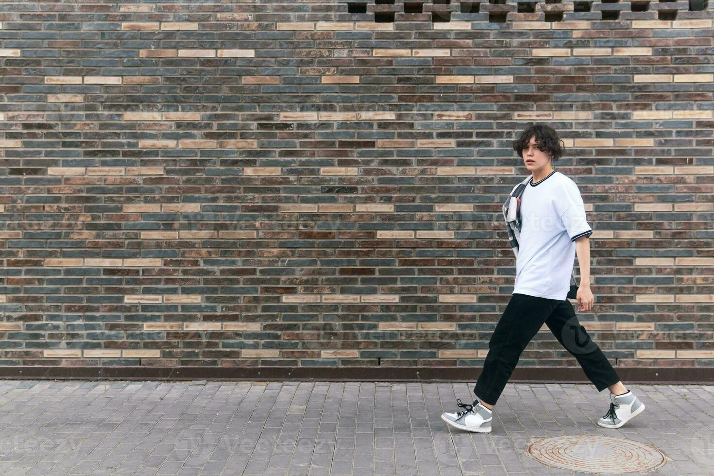 young man walks down the street in front of a brick wall photo