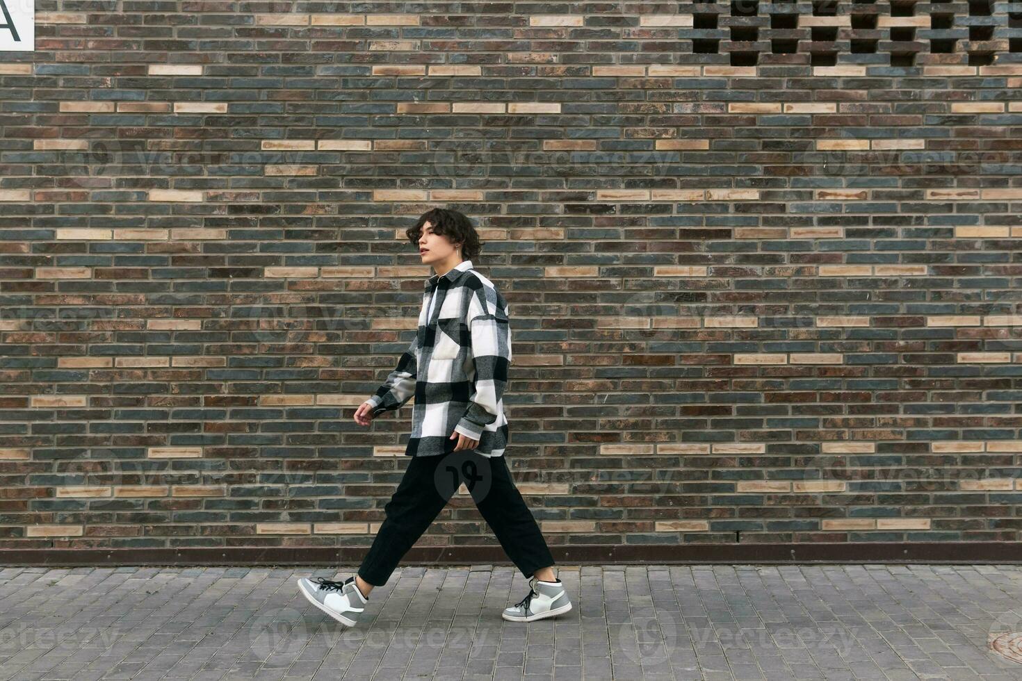 young man walks down the street in front of a brick wall photo