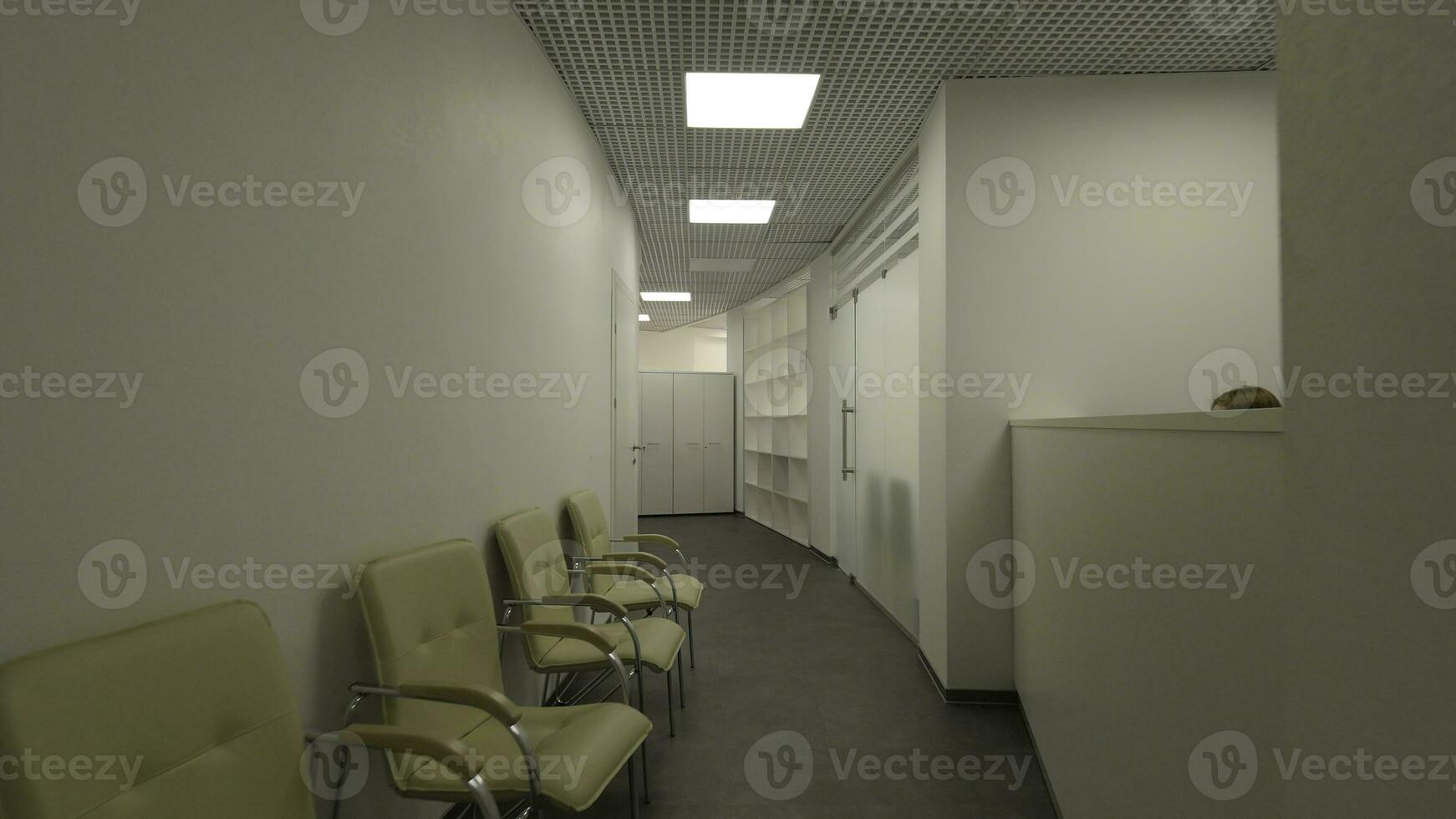 Long, arcuate office hallway and a reception desk. Corridor of a public building with chairs near walls and many doors. photo