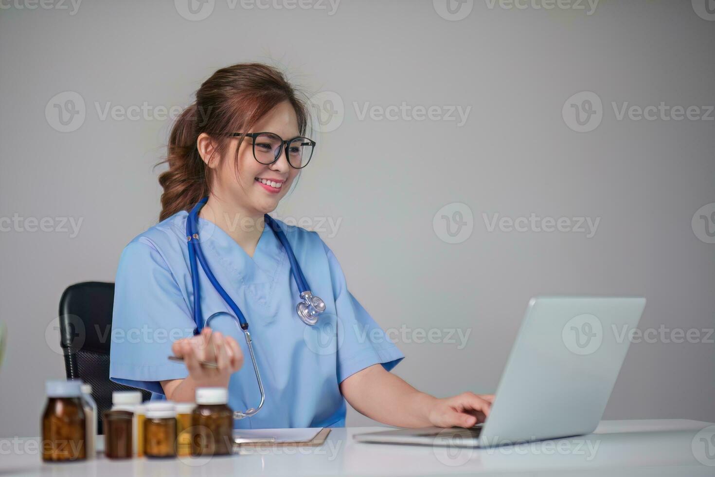 Young Asian doctor in a white medical uniform with a stethoscope using a lab computer and tablet to organize and classify medicines in preparation for administration to patients. photo