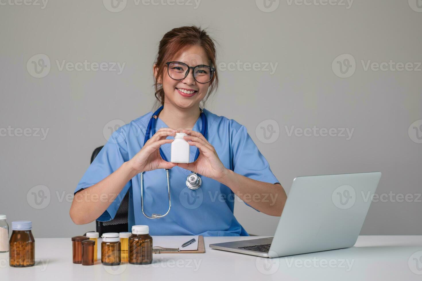 Young Asian doctor in a white medical uniform with a stethoscope using a lab computer and tablet to organize and classify medicines in preparation for administration to patients. photo