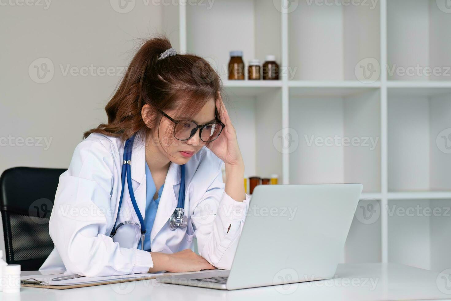 Stressed young female doctor looking at laptop, work related chaos, worried about mistake at work The stressed-out, unhappy medical professional is tired of solving computer problems at work. photo