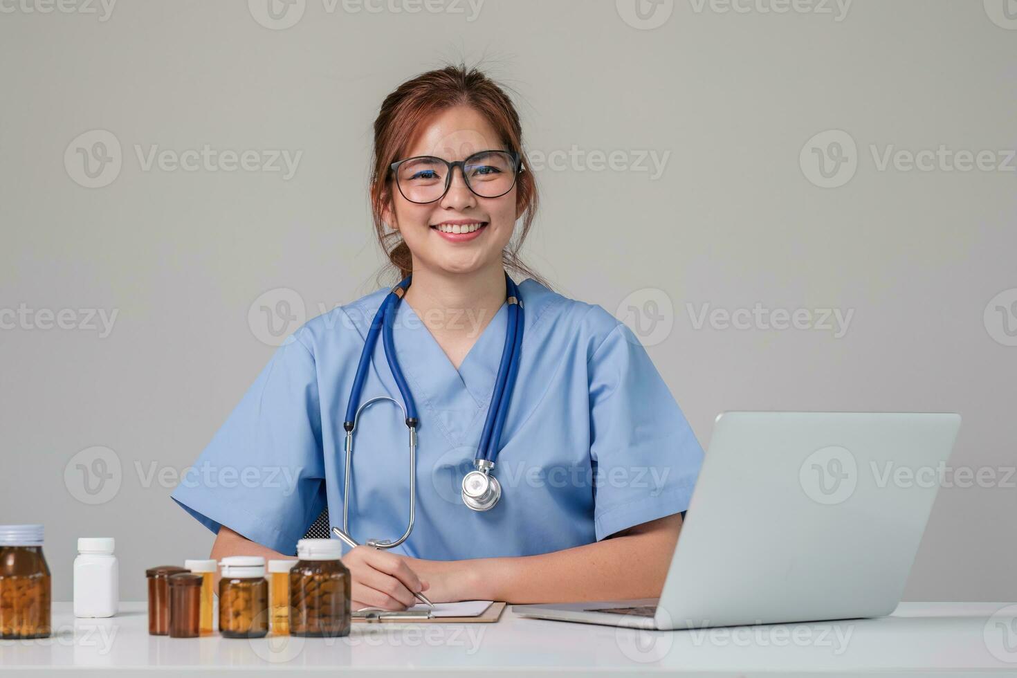 Young Asian doctor in a white medical uniform with a stethoscope using a lab computer and tablet to organize and classify medicines in preparation for administration to patients. photo