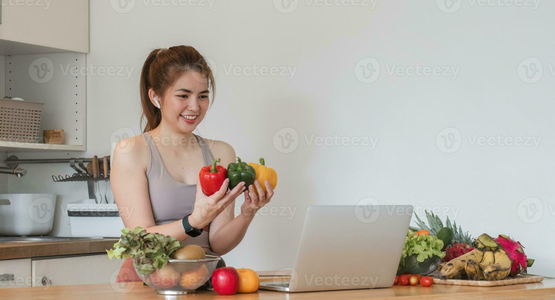 Beautiful Asian woman in workout clothes searches for healthy recipes online on her laptop. while preparing healthy food in the kitchen photo