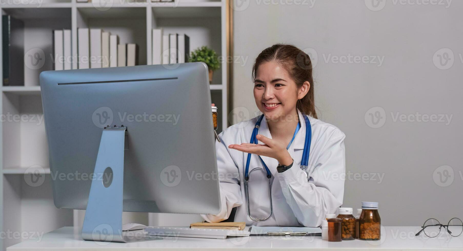 joven hermosa médico participación píldora botella explicando detalles acerca de medicina vía ordenador portátil en línea a clínica foto