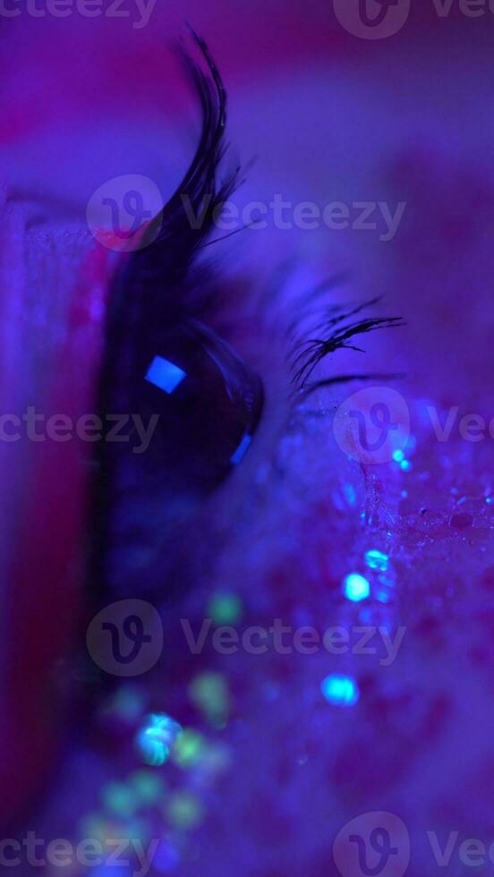 Extreme closeup of female eye with shiny makeup with sparkles illuminated pink-blue neon light photo