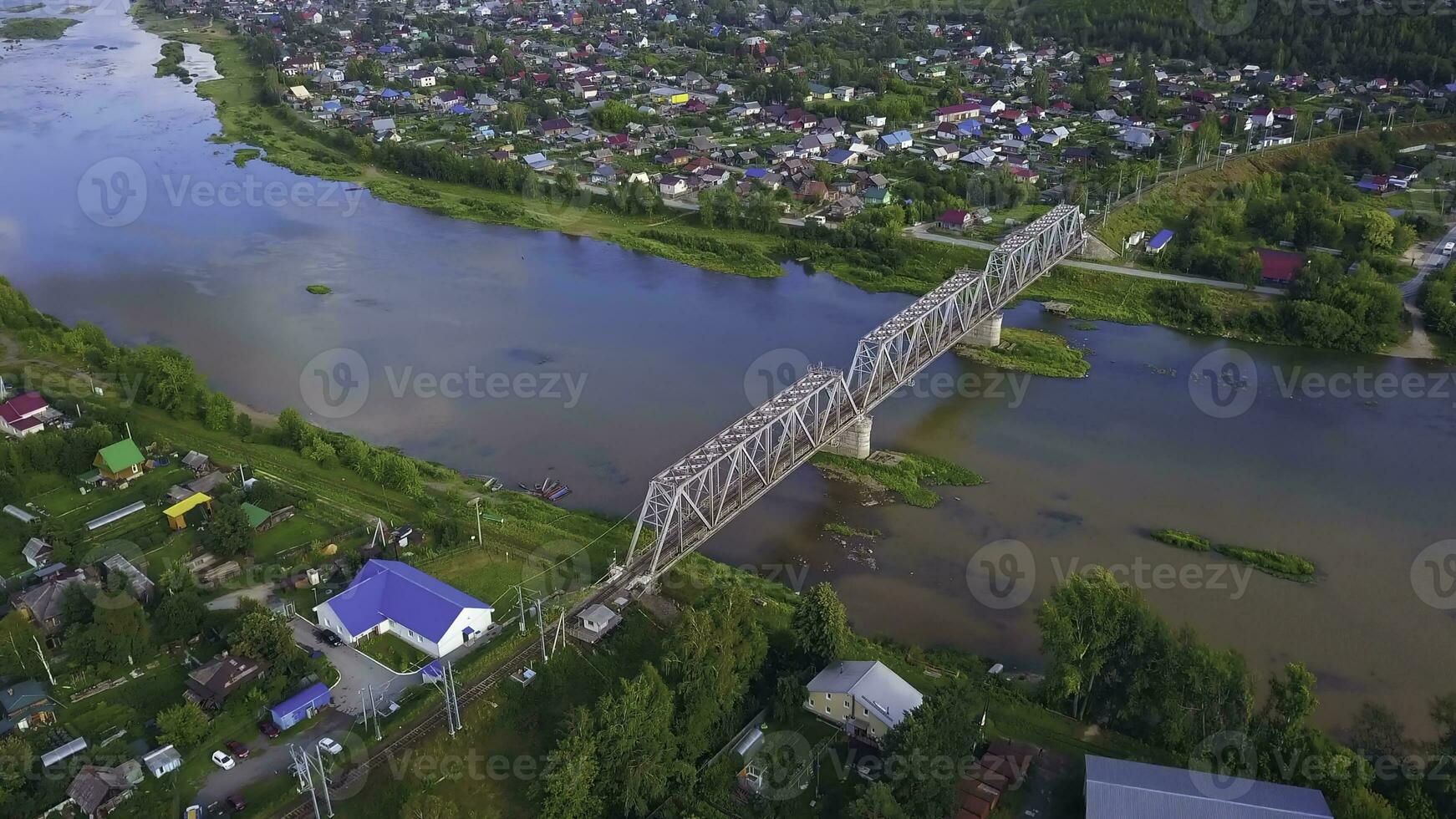 Top view of beautiful landscape of river and town with bridge. Clip. Reflection of sky in river with beautiful bridge on sunny summer day. Landscape with suspension bridge over river in modern town in photo
