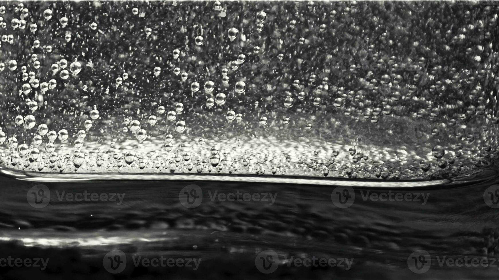 Close-up of small bubbles floating in the glass filled with sparkling water on the dark background. Monochrome photo