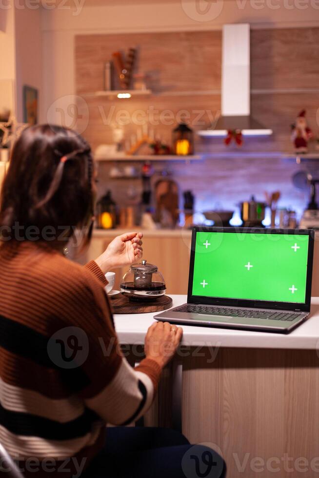 Young adult watching laptop device with green screen technology for mockup template app. Caucasian woman using notebook for digital chroma key isolated display on virtual gadget photo