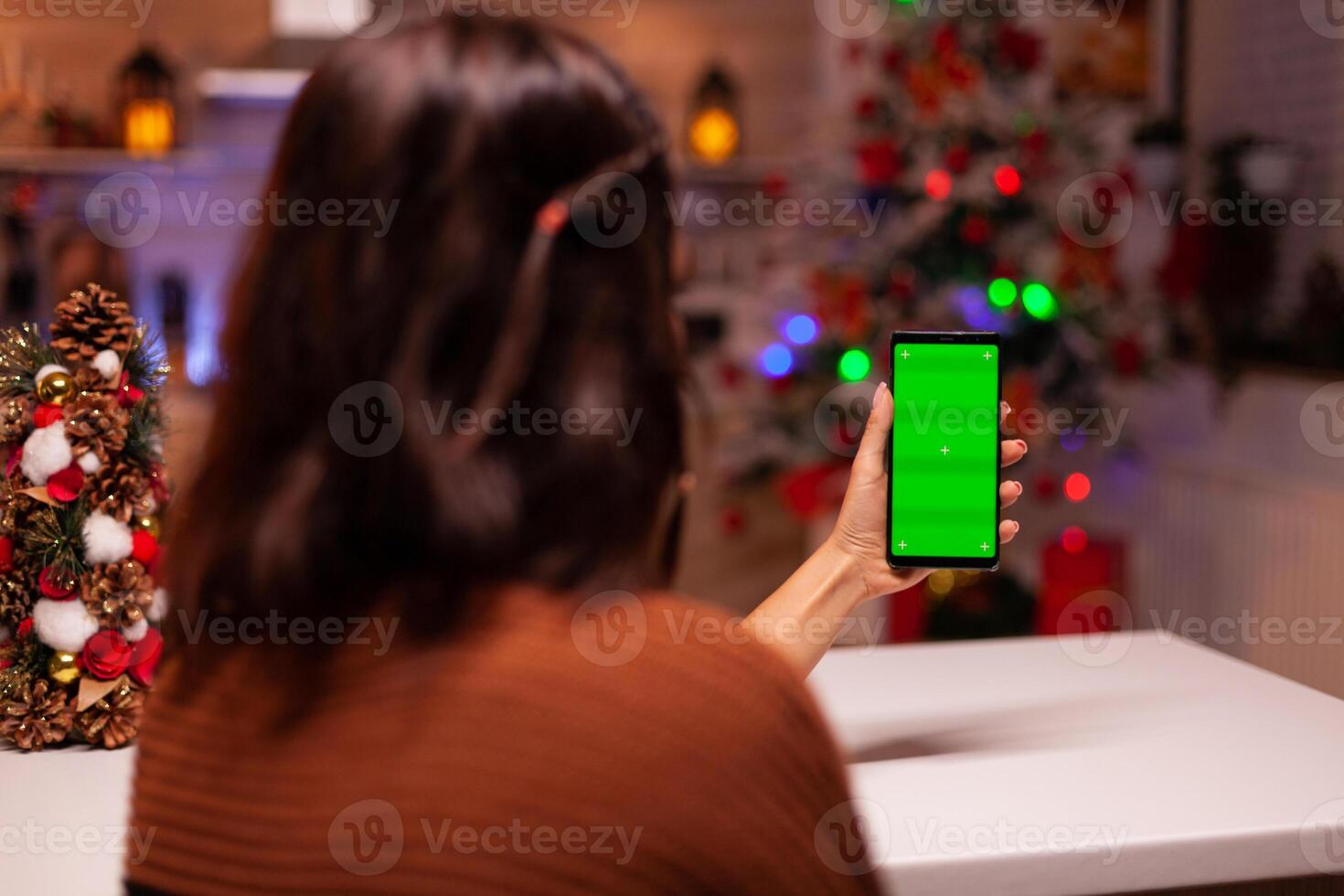 Festive person holding smartphone with green screen for modern technology on mockup template. Caucasian young woman watching digital device with chroma key to view background design photo