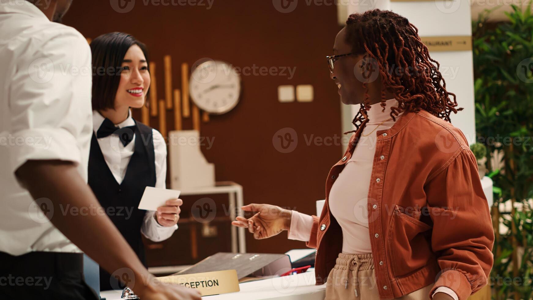 Happy receptionist handing relaxed smiling newlywed couple room access key card during check in process. Cheerful tourists and professional hotel staff chatting in resort lobby photo