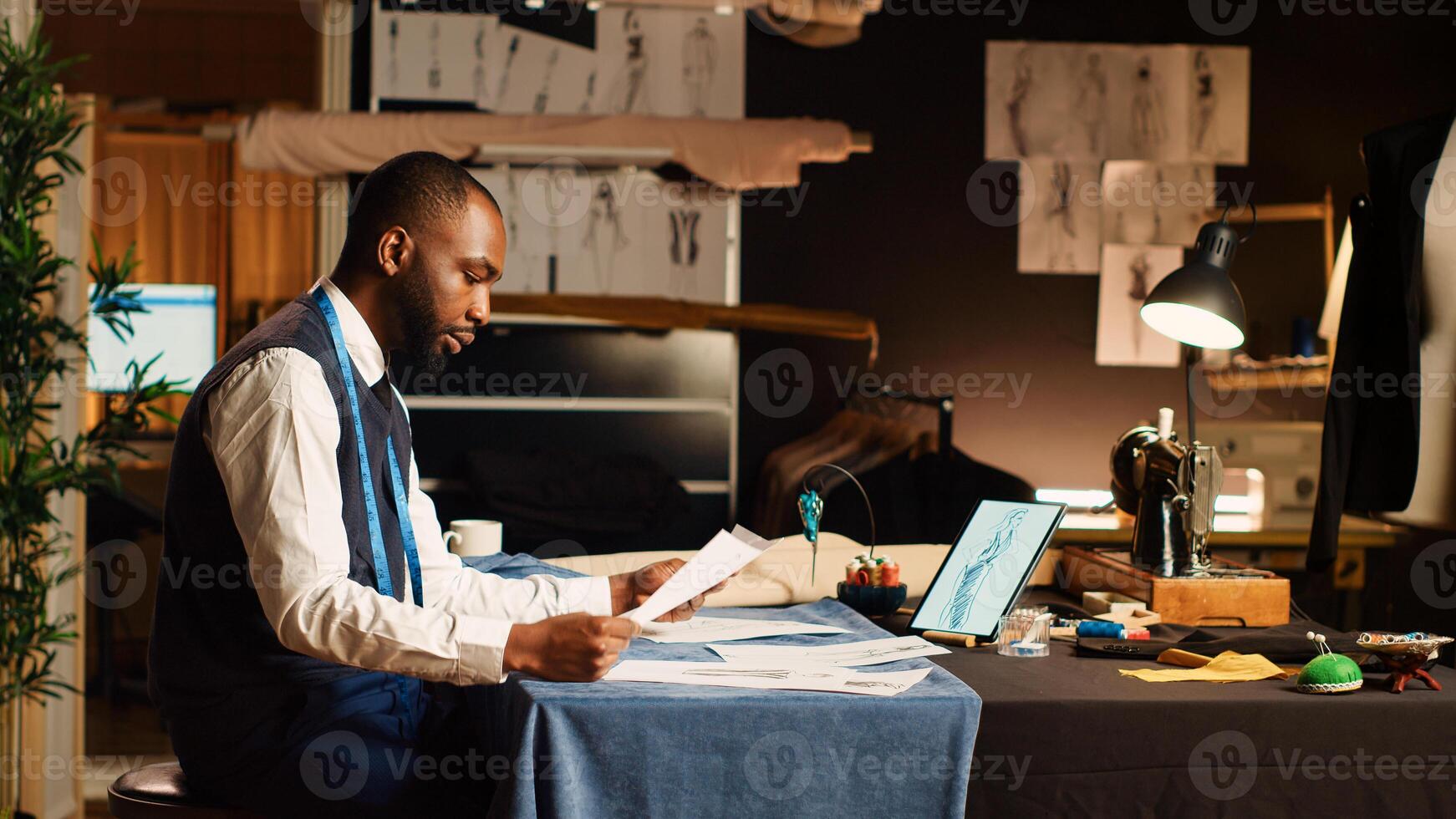 Craftsman checking sketches on laptop, working in atelier to create modern design. Couturier crafting new clothes collection in tailor workshop, small business concept. Tripod shot. photo