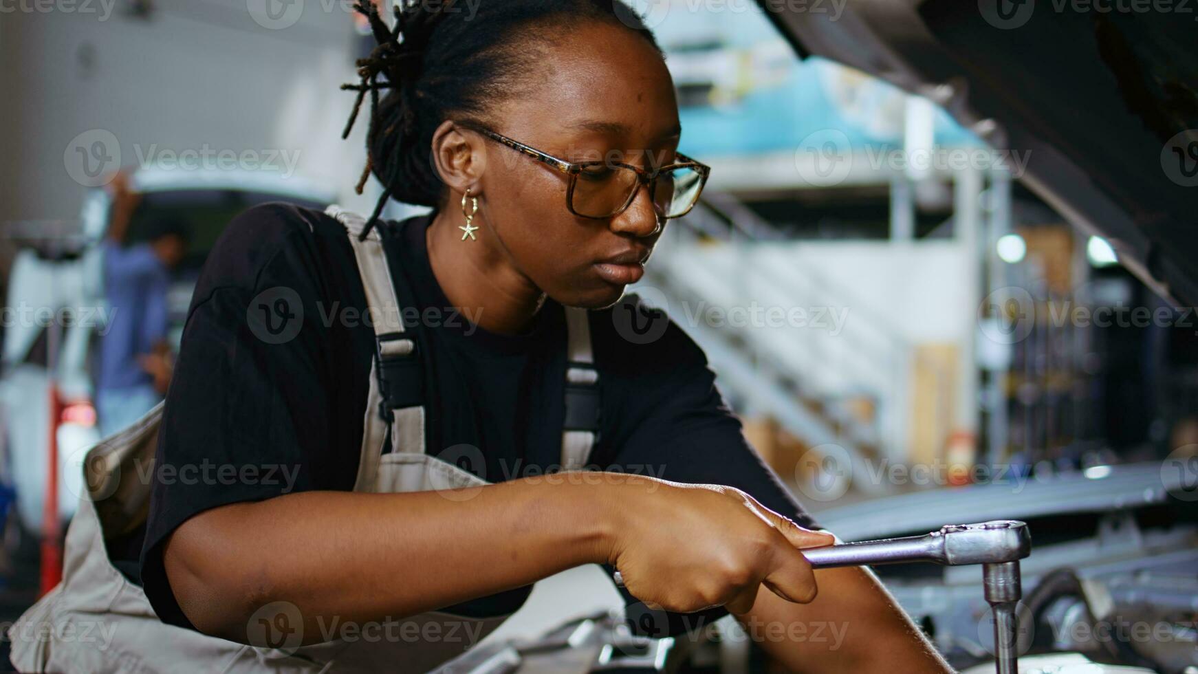 Certified technician in repair shop using torque wrench to tighten screws after checking car parameters during maintenance. African american expert using professional tool in garage to mend vehicle photo