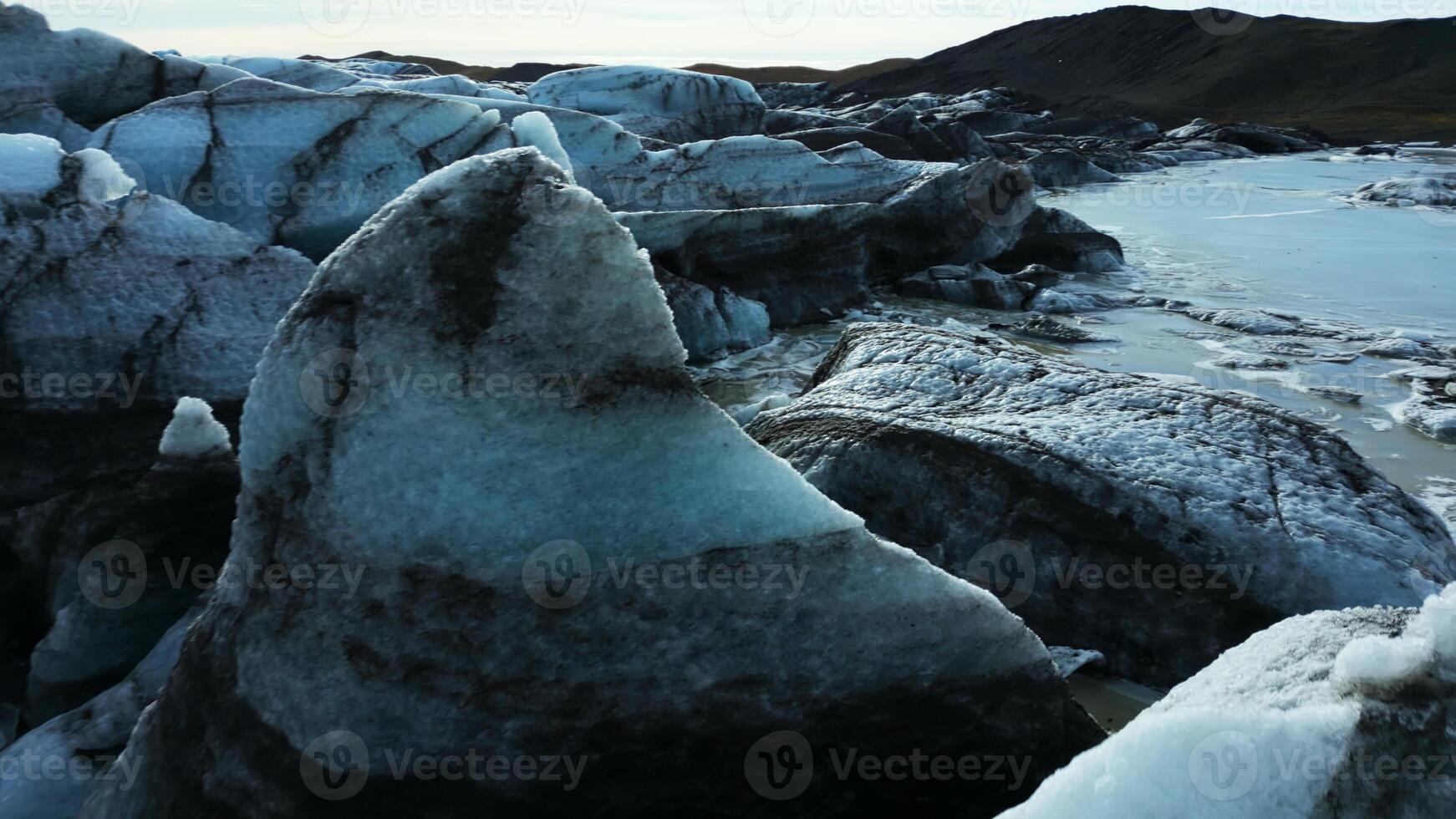 Drone shot of vatnajokull glacier mass, beautiful blue ice blocks with crevasses and icebergs near snowy mountains. Massive icy rocks with frost floating on lake. Slow motion. photo