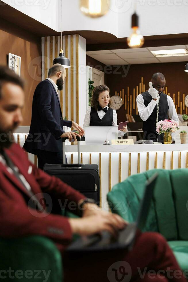 Traveling for work, businessman checking in at hotel reception desk with passport for room reservation confirmation. Guest giving id documents to front desk staff, identification services. photo