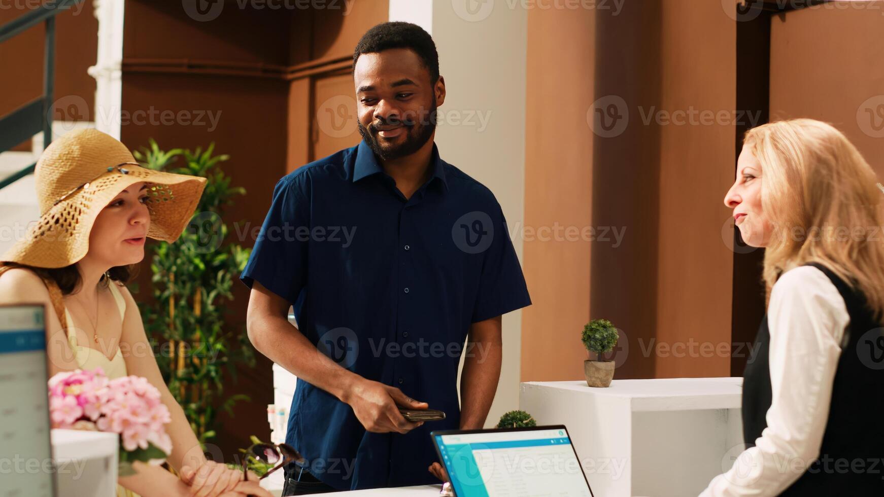 Receptionist looking at passports to register tourists at exotic seaside resort, talking to couple on honeymoon trip. Hotel guests doing check in procedure with front desk staff. Handheld shot. photo