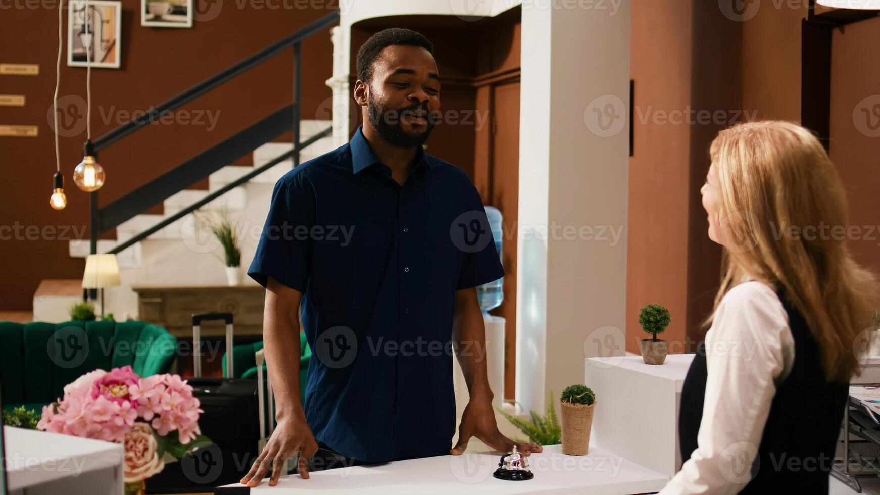 turista registrando a frente escritorio con hotel conserje, hablando a hotel personal acerca de ocio ocupaciones a exótico verano complejo. africano americano invitado llegando en vestíbulo, preparando a cheque en. foto