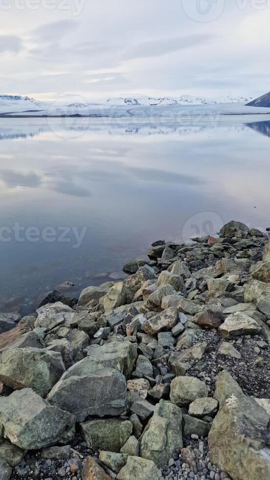 Frosty open water and snowy slopes in icelandic setting, scandinavian frozen lake within nordic iceland landscape. Majestic scenery with rock formations and ice fragments. photo