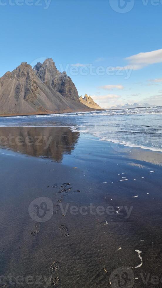 Stone mountain crests meeting the ocean in fantastic icelandic environment with natural black sand beach. Nordic stokksnes peninsula with vestrahorn mountain chain and beachfront, sightseeing. photo