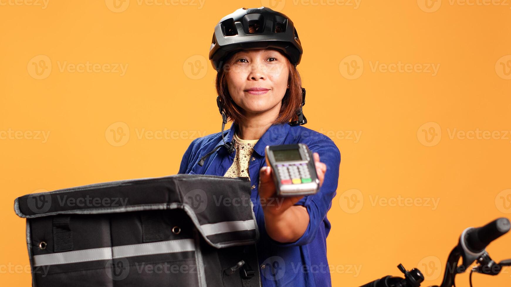 Close up shot of courier isolated over studio background preparing POS terminal for client to purchase ordered food. BIPOC woman providing NFC payment option to customer after succesful delivery photo