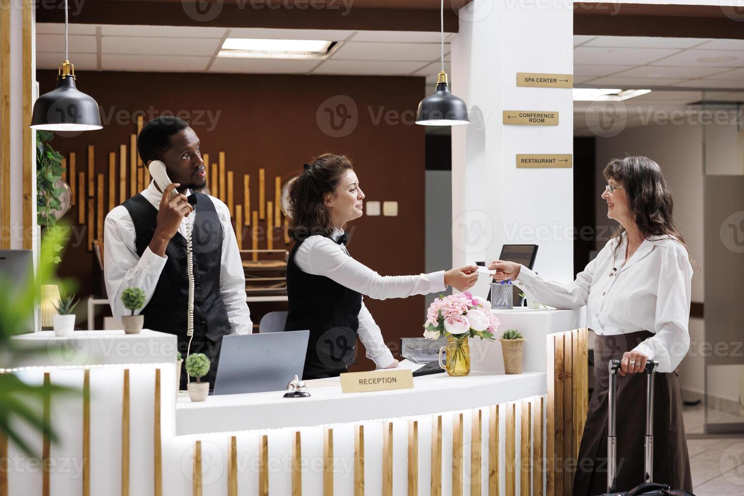 Retired senior woman taking key card from front desk staff and receiving access to accommodation upon arrival at luxury resort. Elderly female tourist finishing check-in procedure at hotel reception. photo