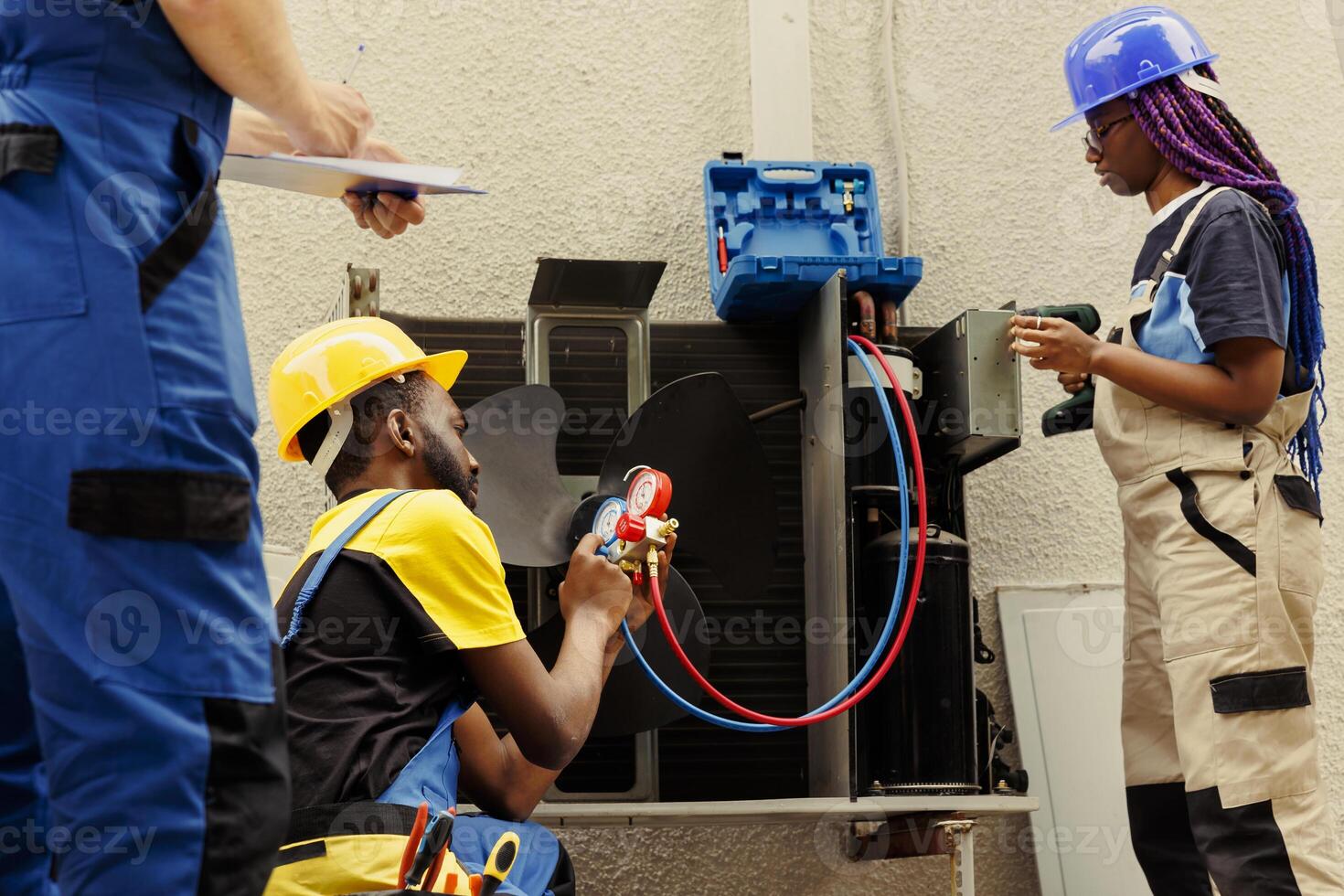Capable electricians expertly refilling freon in outdoor air conditioner while using manifold meters to perfectly measure the pressure in HVAC system, ensuring required cooling performance photo
