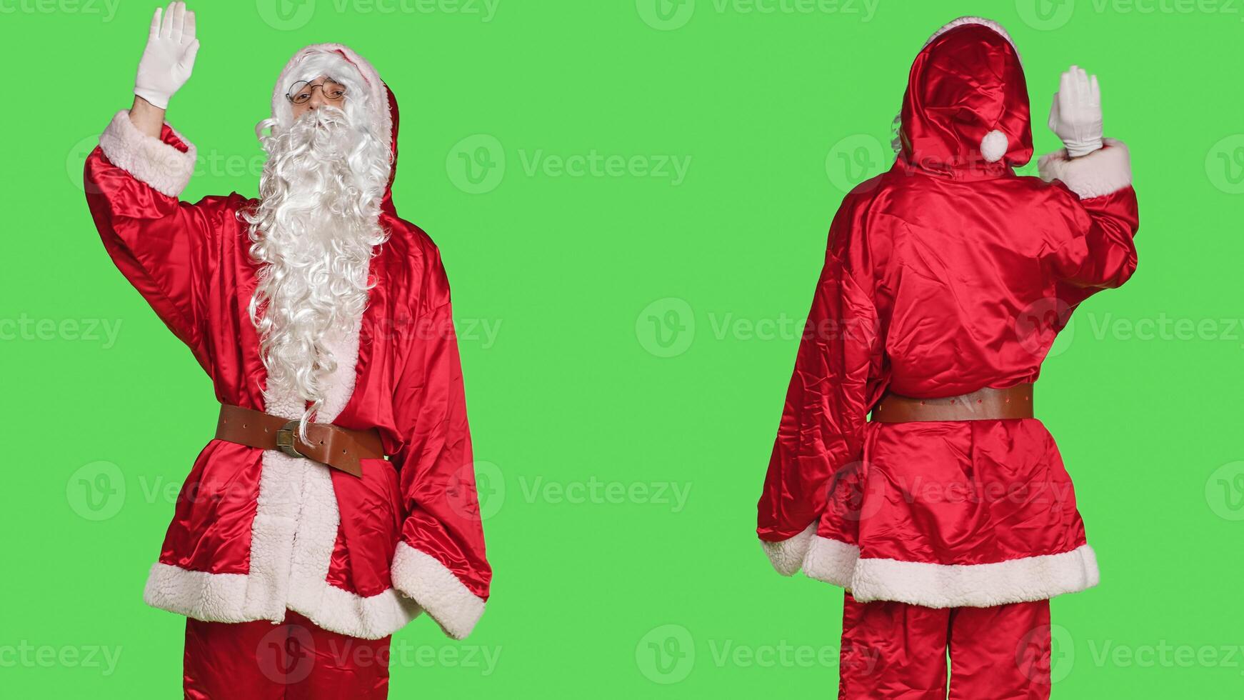 Saint nick enbodiment greeting people, wearing festive seasonal costume and waving hello on greenscreen backdrop. Young adult celebrating christmas eve in red suit, smiling at camera. photo
