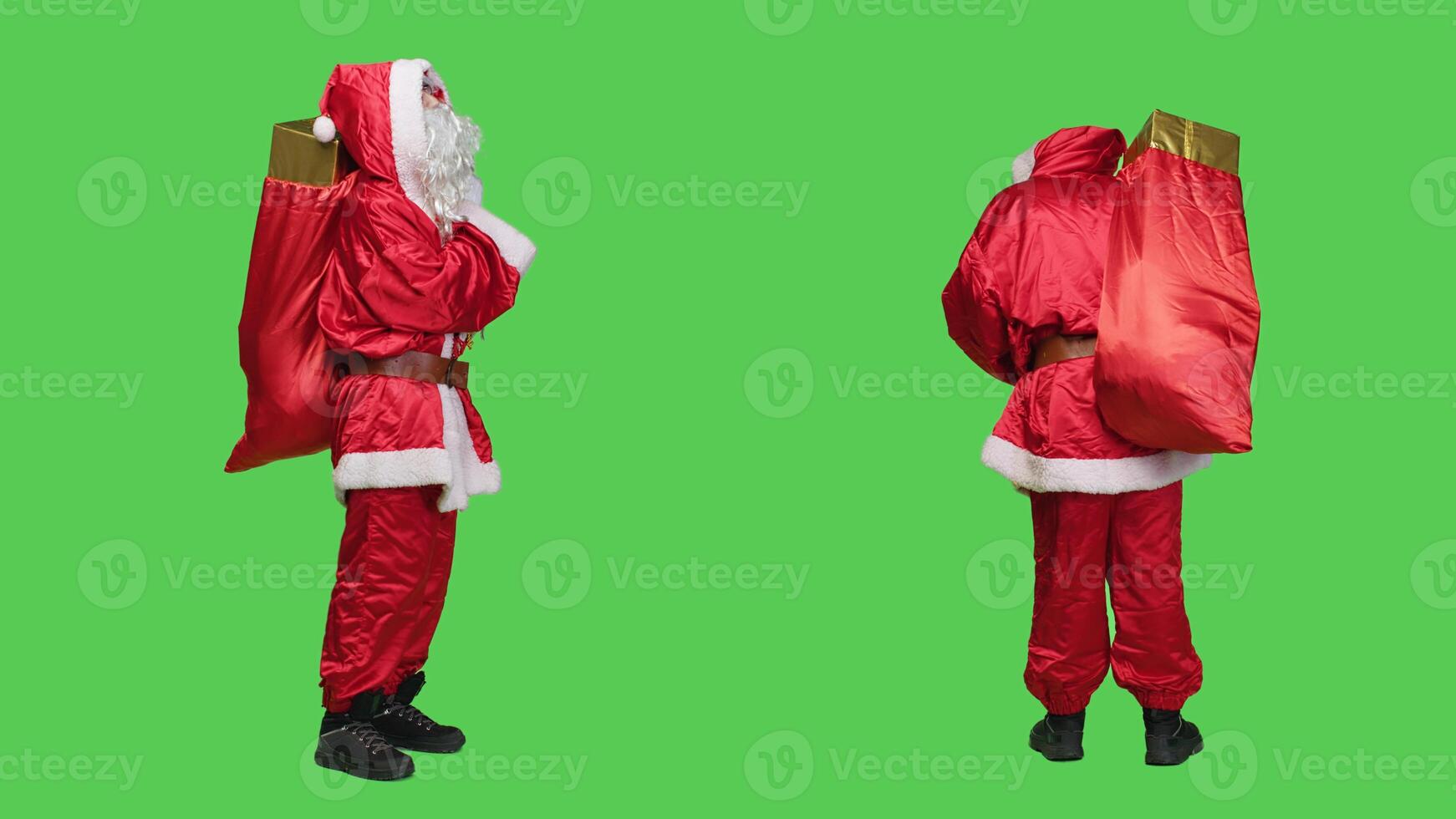 Saink nick in suit looking around, carrying big red bag full of gift boxes over full body greenscreen backdrop. Young person dressed as santa spreading christmas holiday spirit, presents for kids. photo