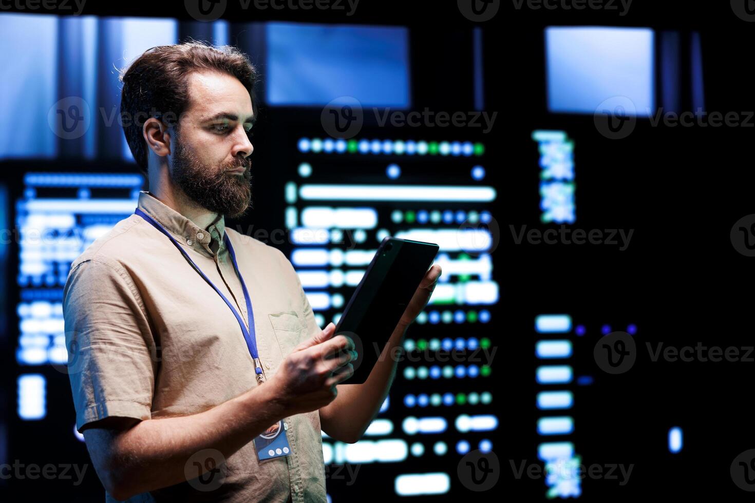 Electrician doing annual system querying, imputing data on tablet of required refurbishing in server rows housing advanced data storage equipment supporting complex computing operations photo