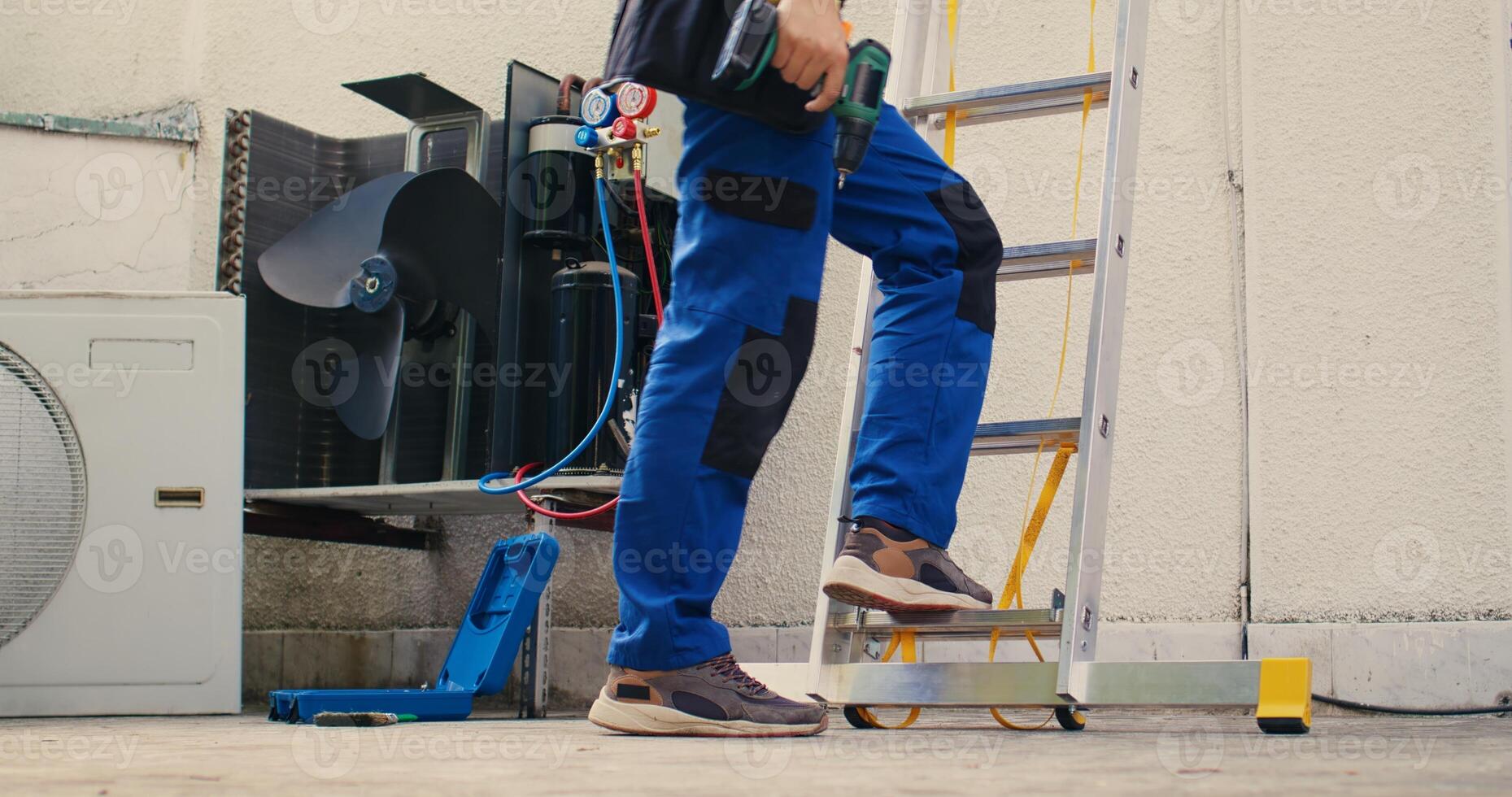 Meticulous mechanic in professional uniform with technical equipment climbing folding ladder to do maintenance on rooftop hvac system. Professional worker commissioned to check up on air conditioner photo