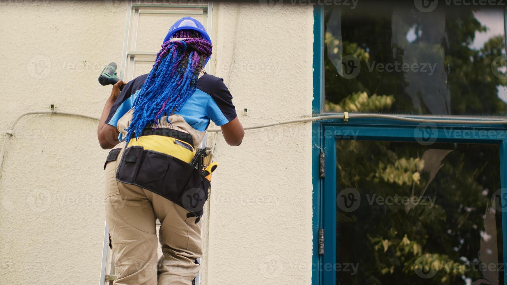 Adept repairman holding electric drill, stepping down from folding ladder after finishing check up on rooftop hvac system. Proficient worker at the end of maintenance assignment photo