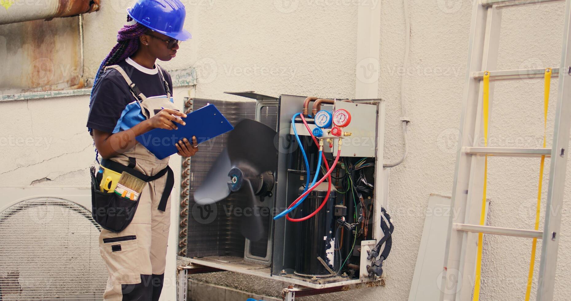 Professional wireman commissioned for external air conditioner routine check up, writing findings on clipboard. Specialist doing hvac system investigation of damaged parts photo