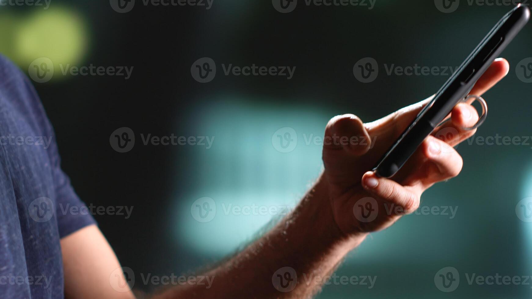 Young man walking around town at nighttime, using mobile phone under streetlamps strolling near urban buildings. Person enjoying walk texting messages on sidewalk. Handheld shot. Close up. photo