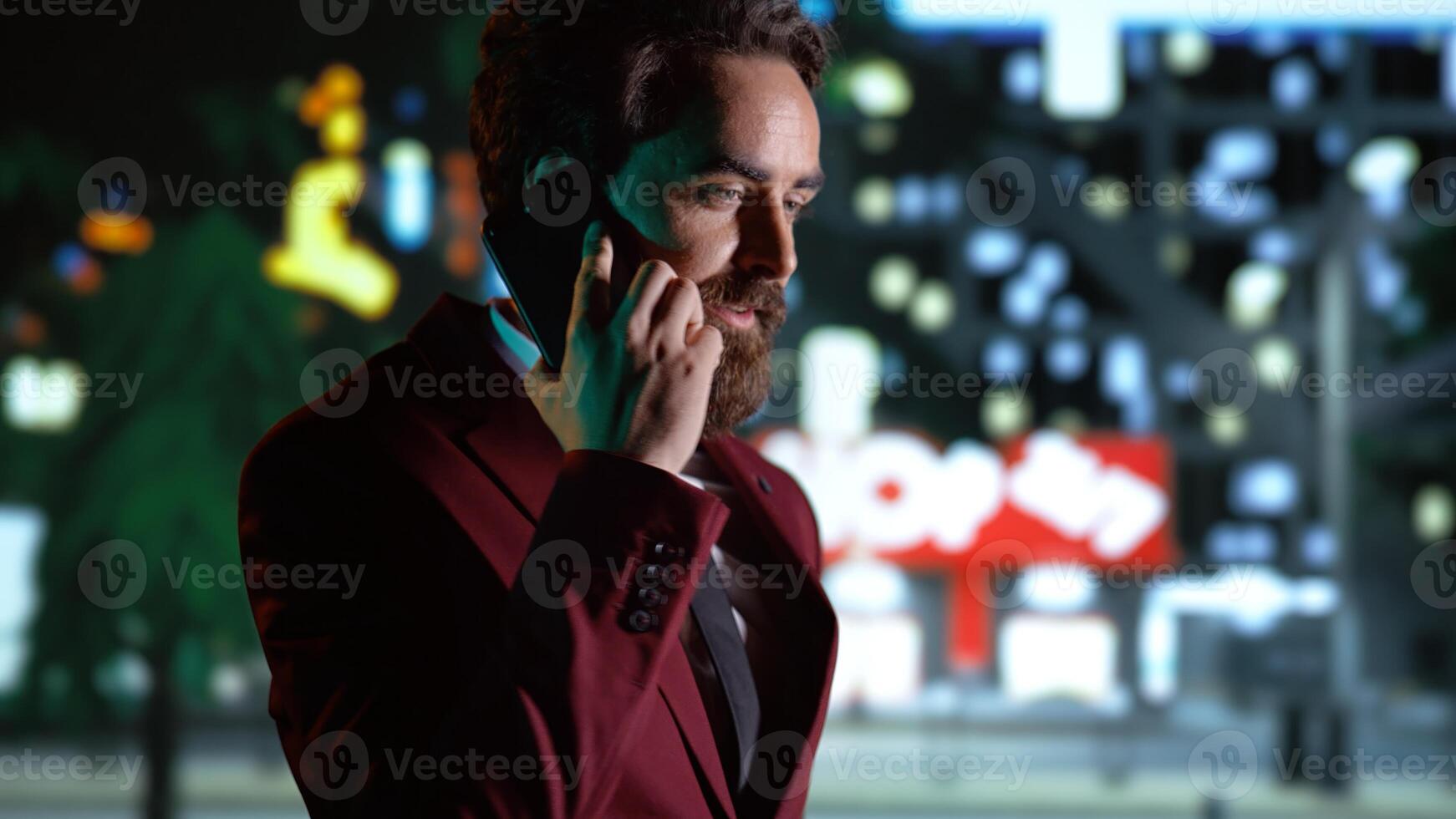 Businessman on phone call strolling around city, enjoying night walk while he talks on smartphone. Person admiring skyscrapers, walking near busy town center district on promenade. Handheld shot. photo